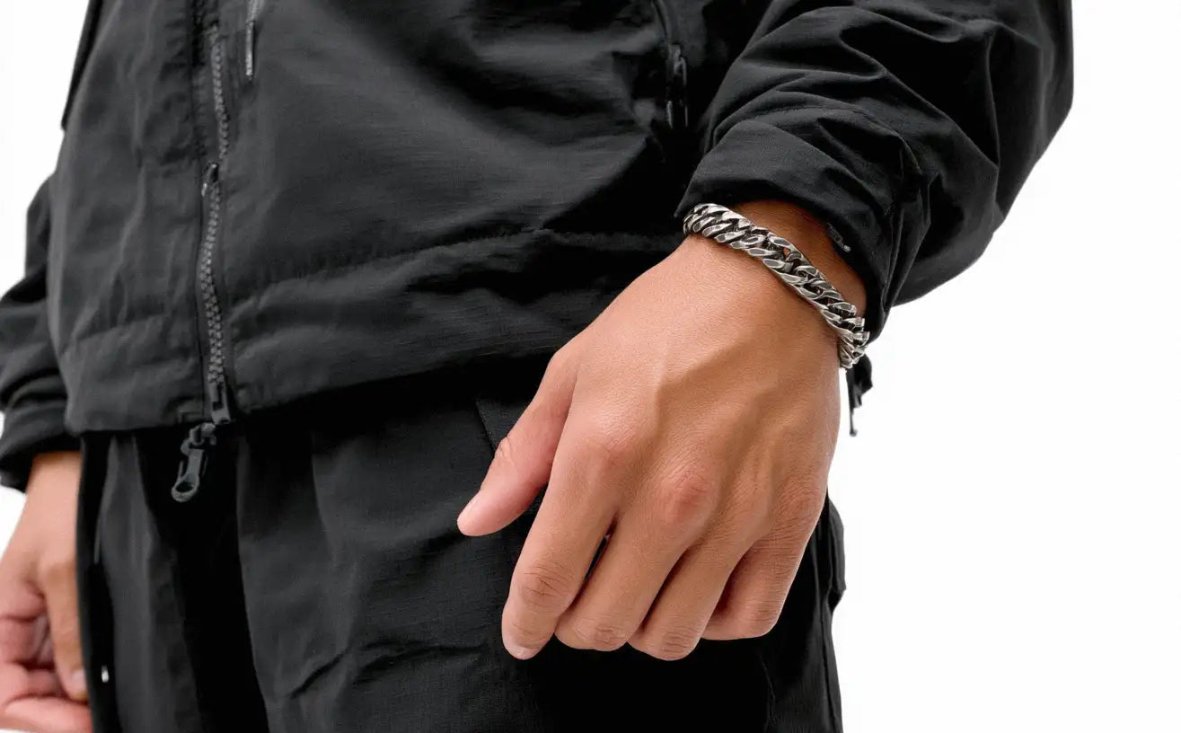 Close-up view of a person's arm wearing a thick, classic curb chain Stainless Steel Bracelet with a black jacket.
