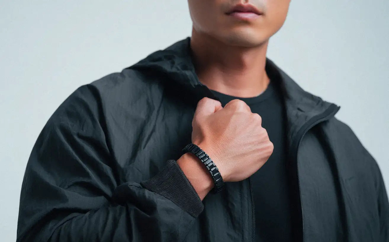 A man in a black jacket and t-shirt, subtly displaying a dark, rectangular link Stainless Steel Bracelet.