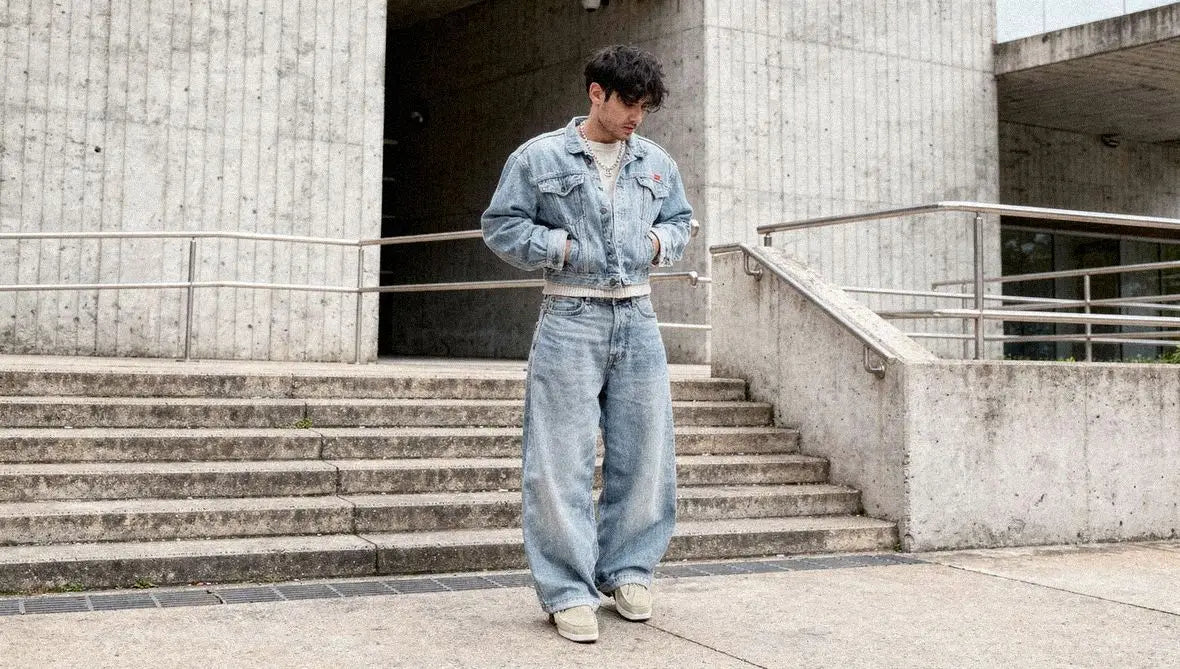 Man in a light wash denim jacket and cream knit layers light blue barrel jeans with beige low top sneakers