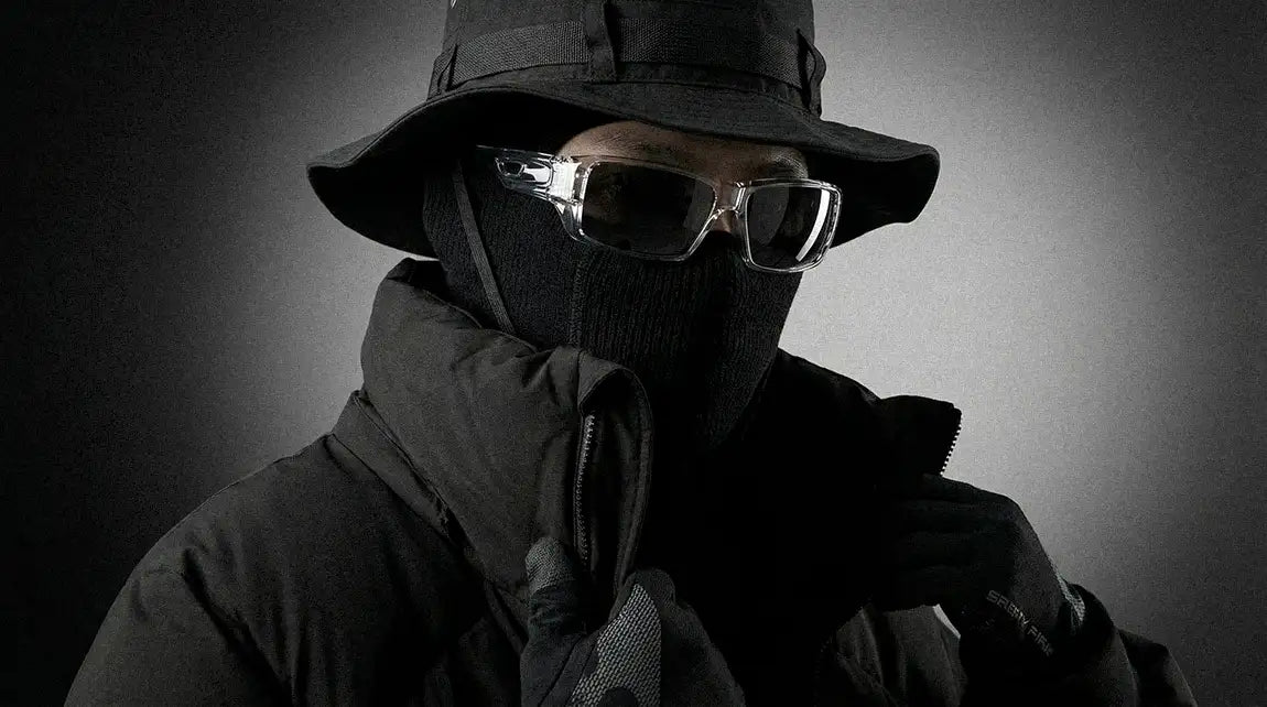 Person in tactical techwear outfit wearing clear-frame futuristic sunglasses with face mask and bucket hat for cyberpunk look
